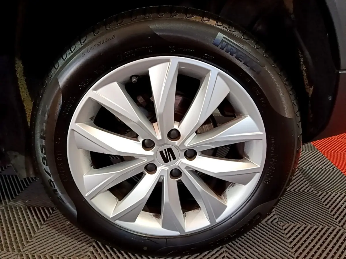 Gros plan sur la jante alliage argentée avec logo SEAT, montée sur pneu Pirelli, véhicule gris clair visible en arrière-plan.