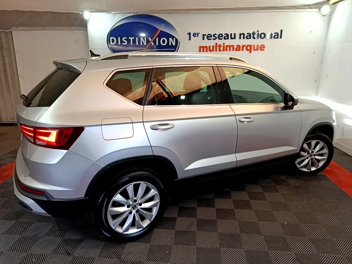Vue 3/4 arrière droite d'un SEAT Ateca gris clair 2022 avec jantes alliage et feux LED allumés en intérieur.