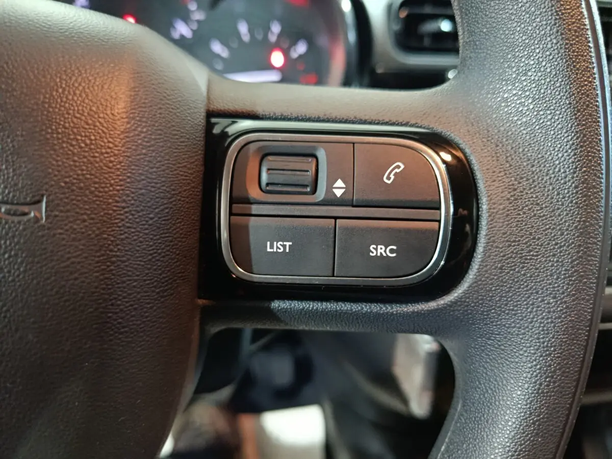 Gros plan sur les commandes gauche du volant noir de la Citroën C3 2024 BlueHDi, avec boutons LIST et SRC visibles.