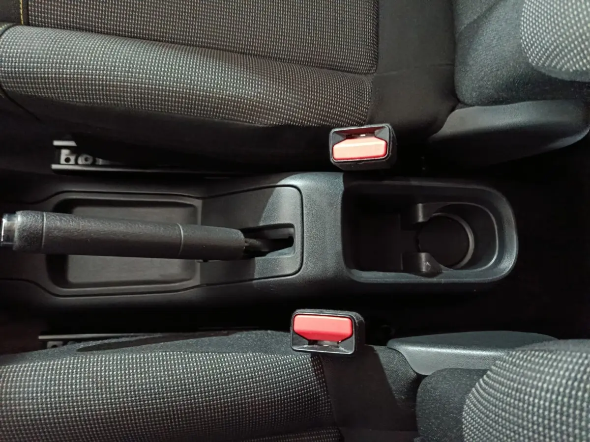 Vue plongeante sur la console centrale noire de la Citroën C3 2024 avec frein à main manuel et deux ceintures rouges.