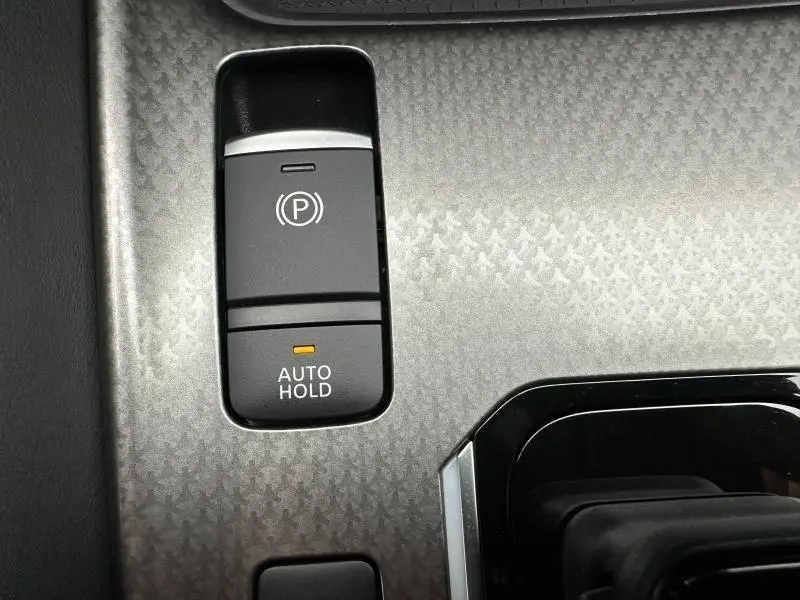 Gros plan sur la console centrale du Nissan Qashqai Hybrid e-POWER 2025, bouton frein à main électronique et Auto Hold sur finition Blanc Nacré.