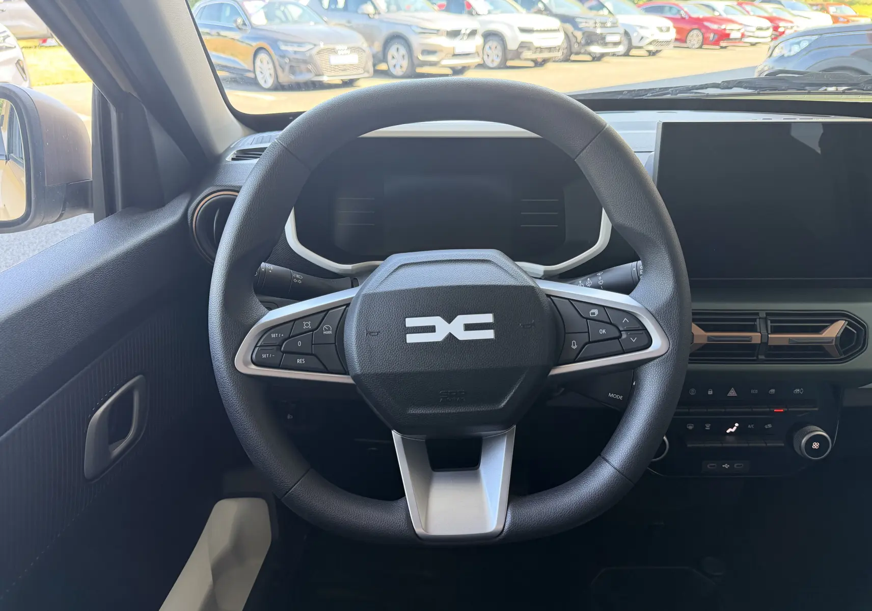 Vue intérieure centrée sur le volant cuir multifonction du Dacia Spring 65 Extreme beige Safari avec tableau de bord digital.