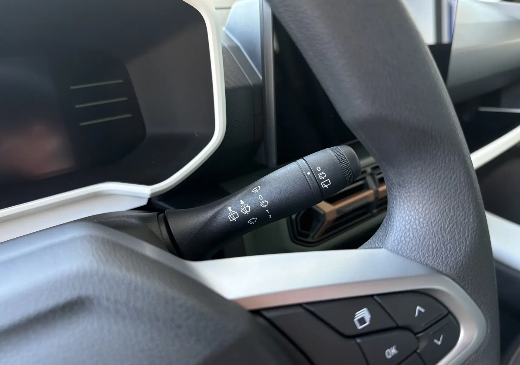 Gros plan sur la commande d’essuie-glace à gauche du volant noir dans l’habitacle du Dacia Spring Beige Safari 2026.