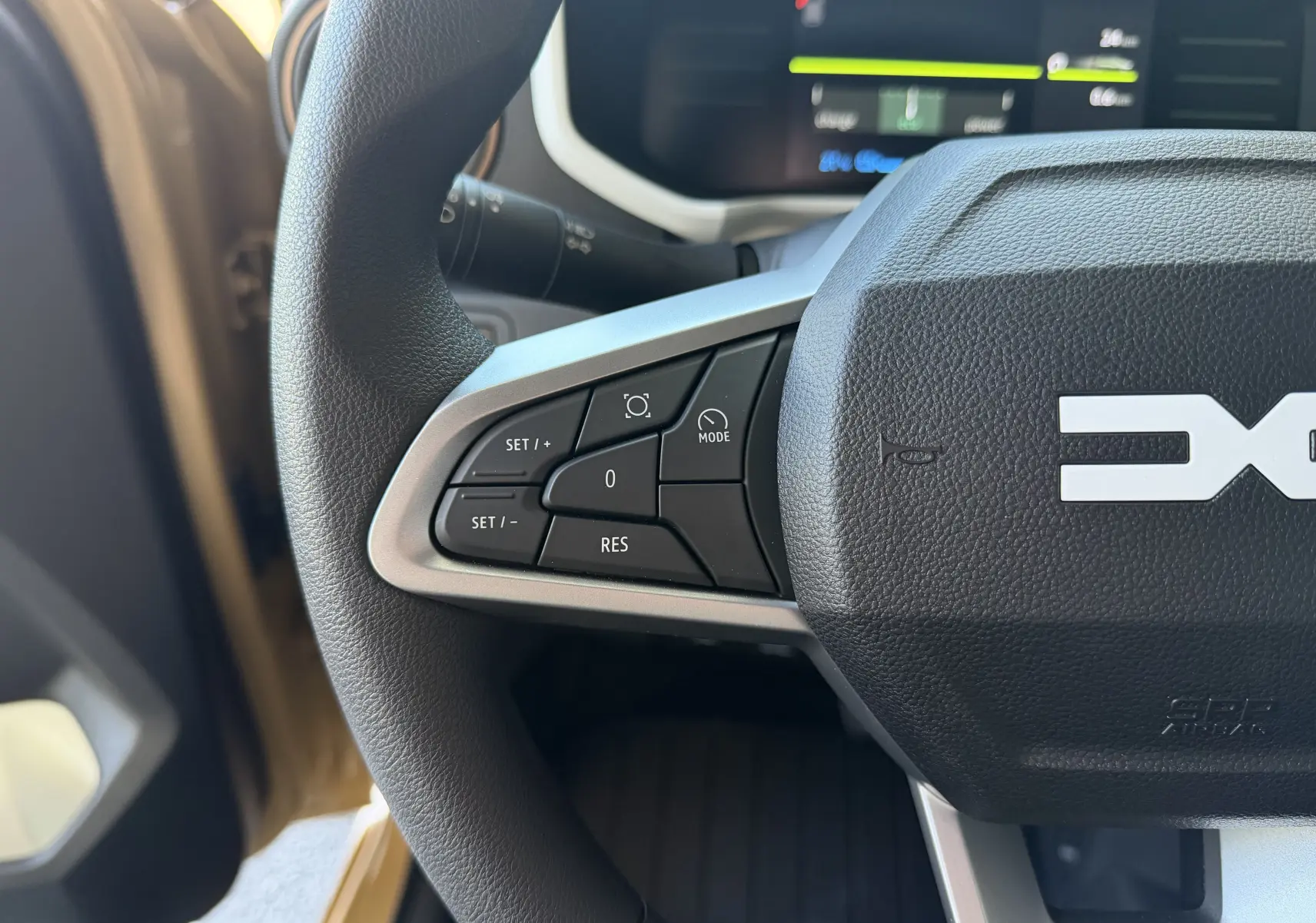 Gros plan sur le volant côté gauche du Dacia Spring 65 Extreme beige Safari avec commandes de régulateur et tableau de bord numérique.