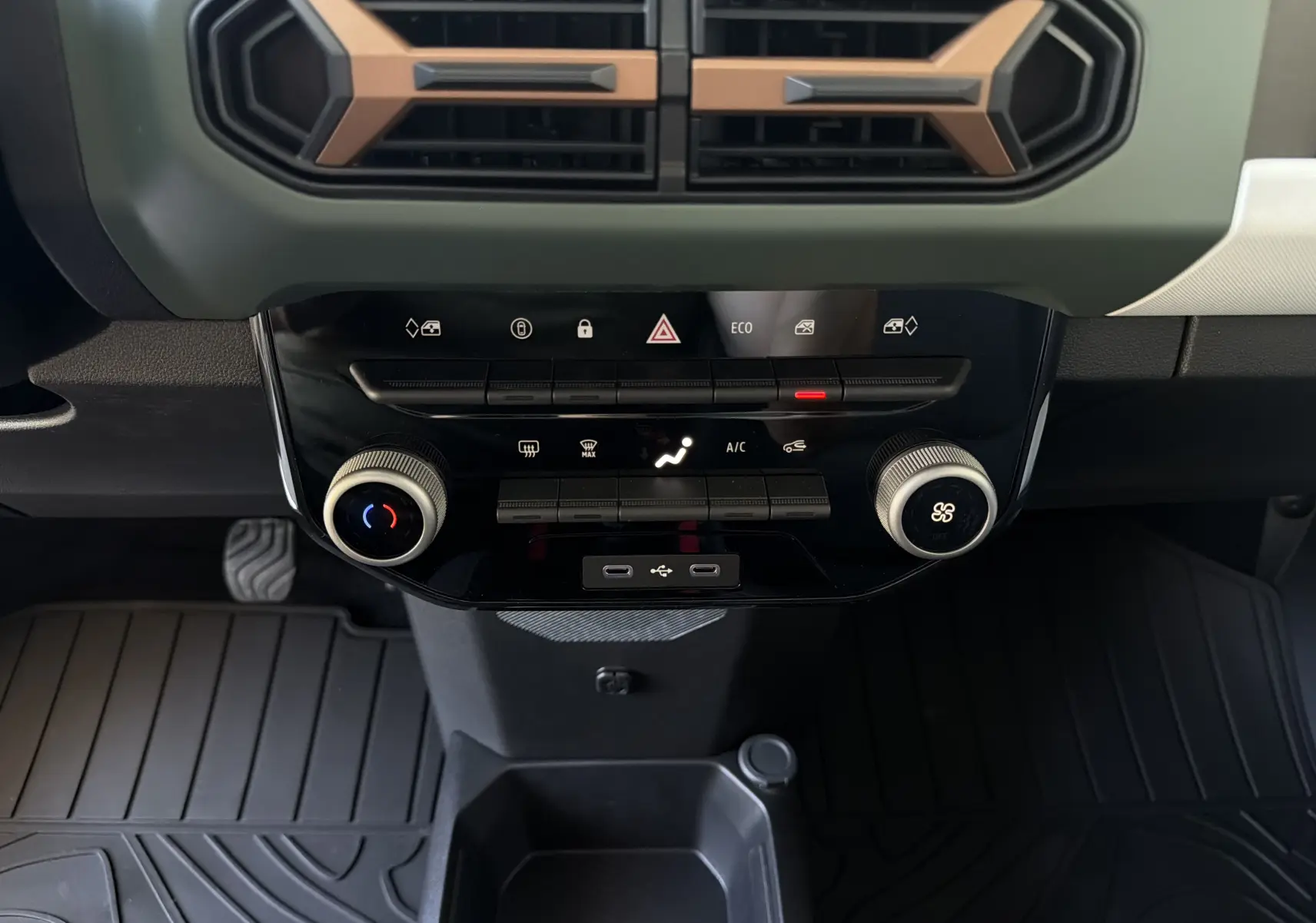 Vue rapprochée de la console centrale de la Dacia Spring 65 Extreme 2026 beige Safari, avec commandes climatisation et prises USB.