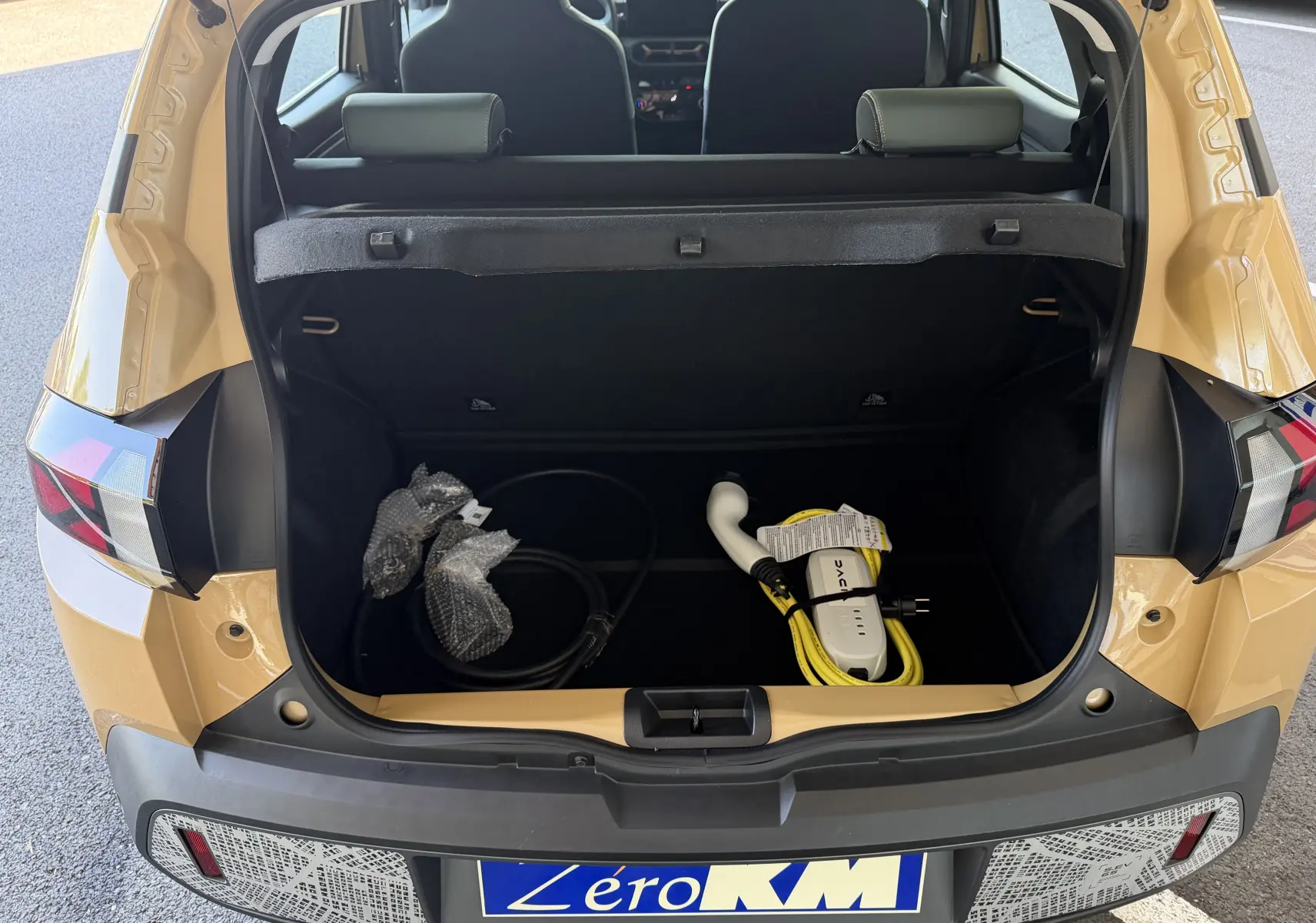Vue arrière ouverte du coffre beige safari du Dacia Spring 65 Extreme 2026, avec câble de recharge électrique visible.