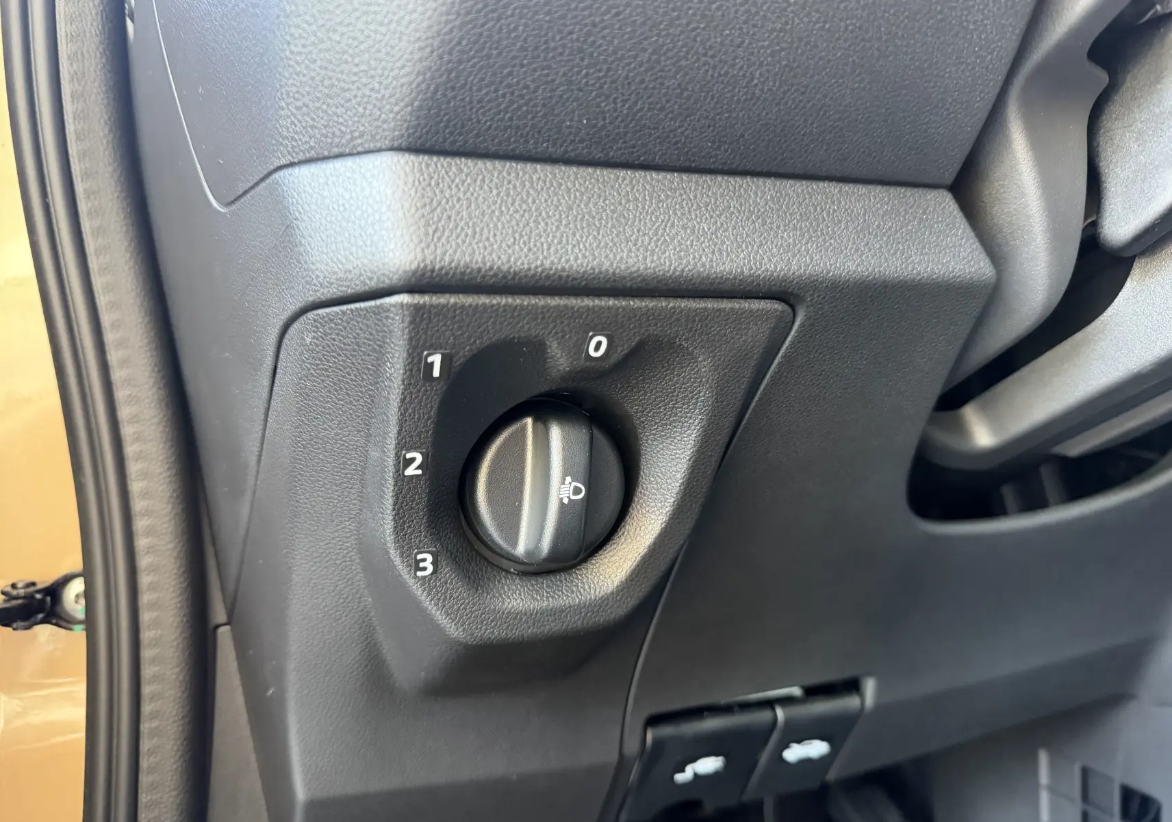 Gros plan sur le réglage des phares dans l’habitacle noir d’une Dacia Spring 65 Extreme beige Safari, côté gauche.
