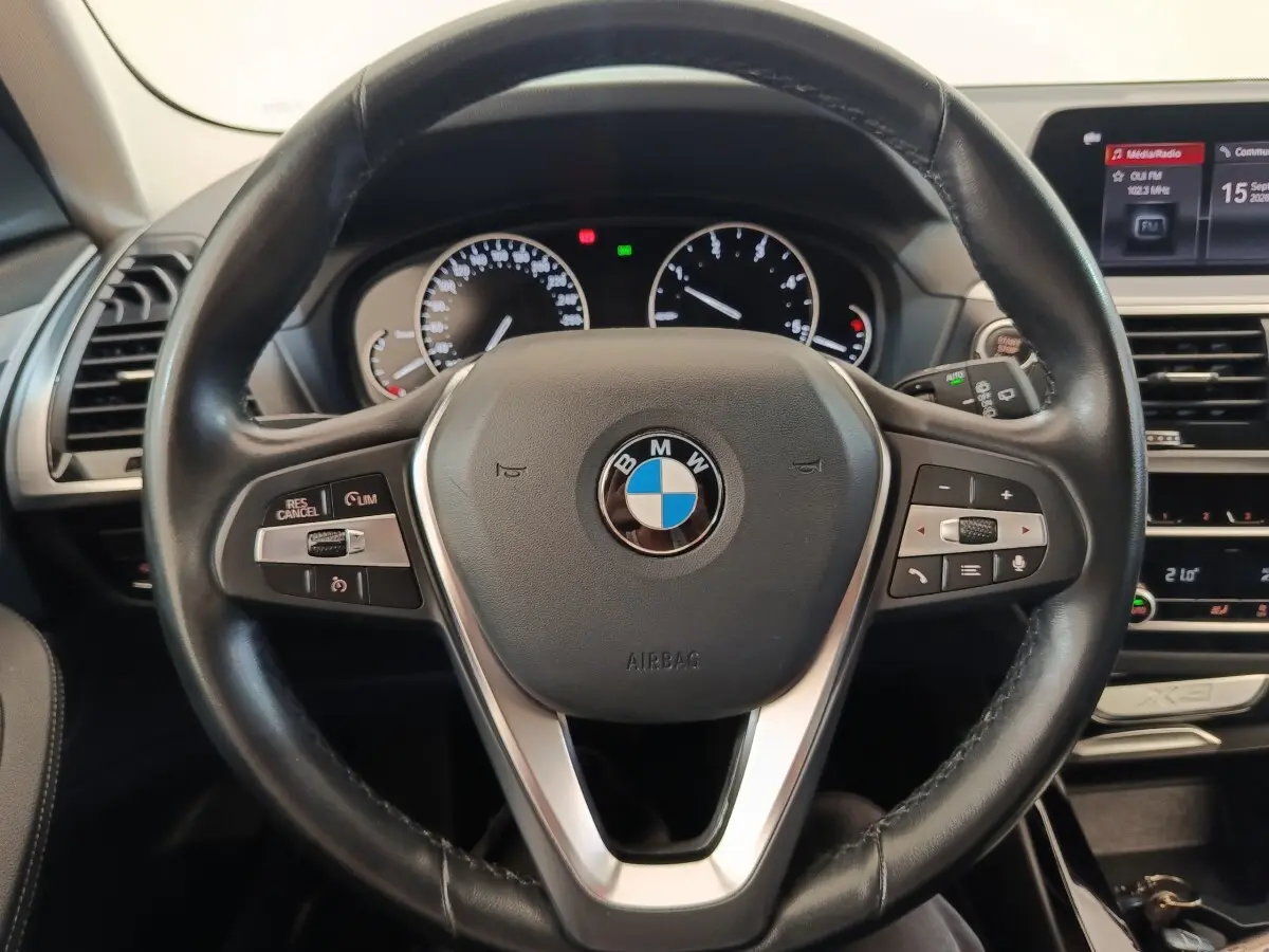 Vue rapprochée du volant cuir et alu multifonctions d’un BMW X3 2020 avec tableau de bord et écran central visibles.