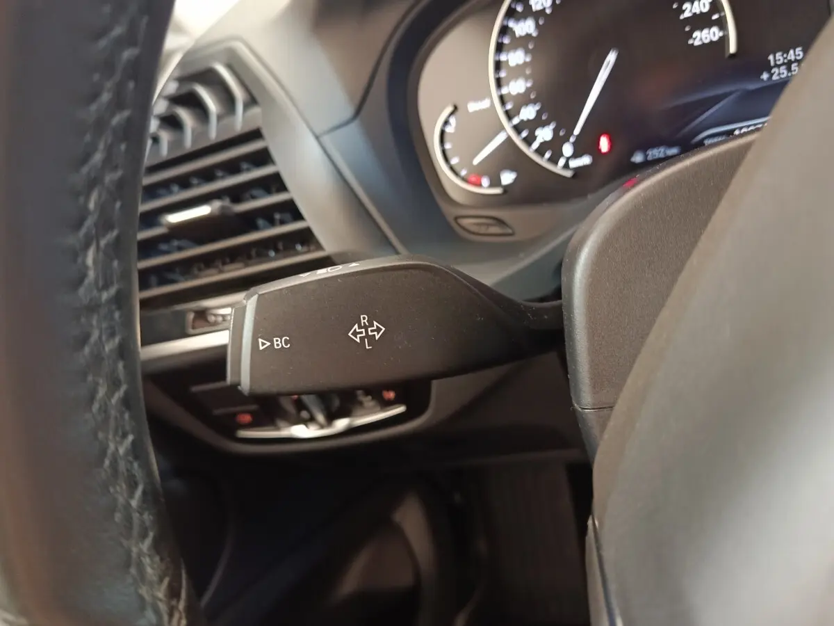 Gros plan sur la manette de clignotant à gauche du volant cuir d’une BMW X3 gris clair, tableau de bord en arrière-plan.