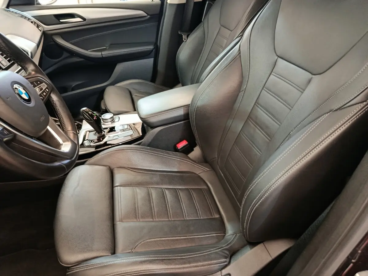 Vue intérieure côté conducteur d'une BMW X3 2020, sièges cuir noirs et volant multifonctions alu et cuir.
