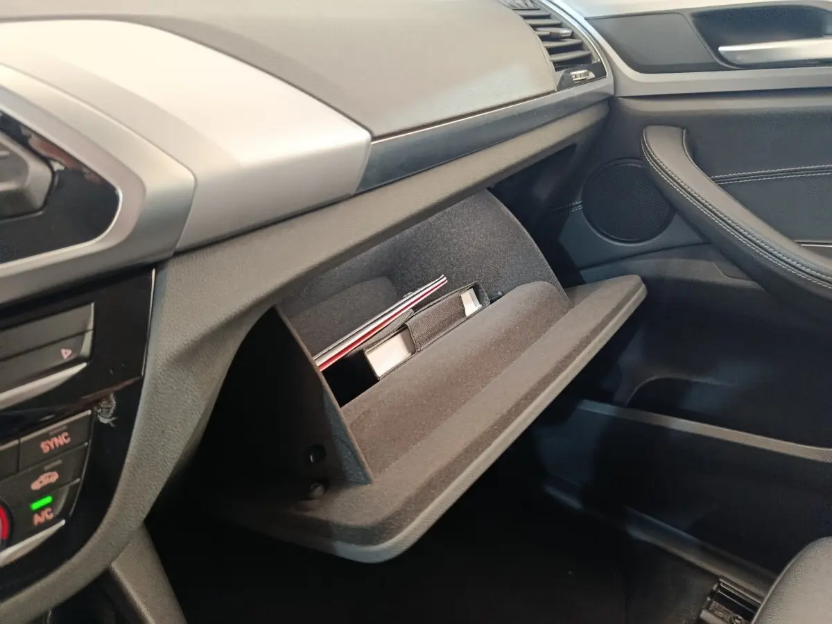 Intérieur BMW X3 2020 côté passager, boîte à gants ouverte avec documents, finition noire et grise.