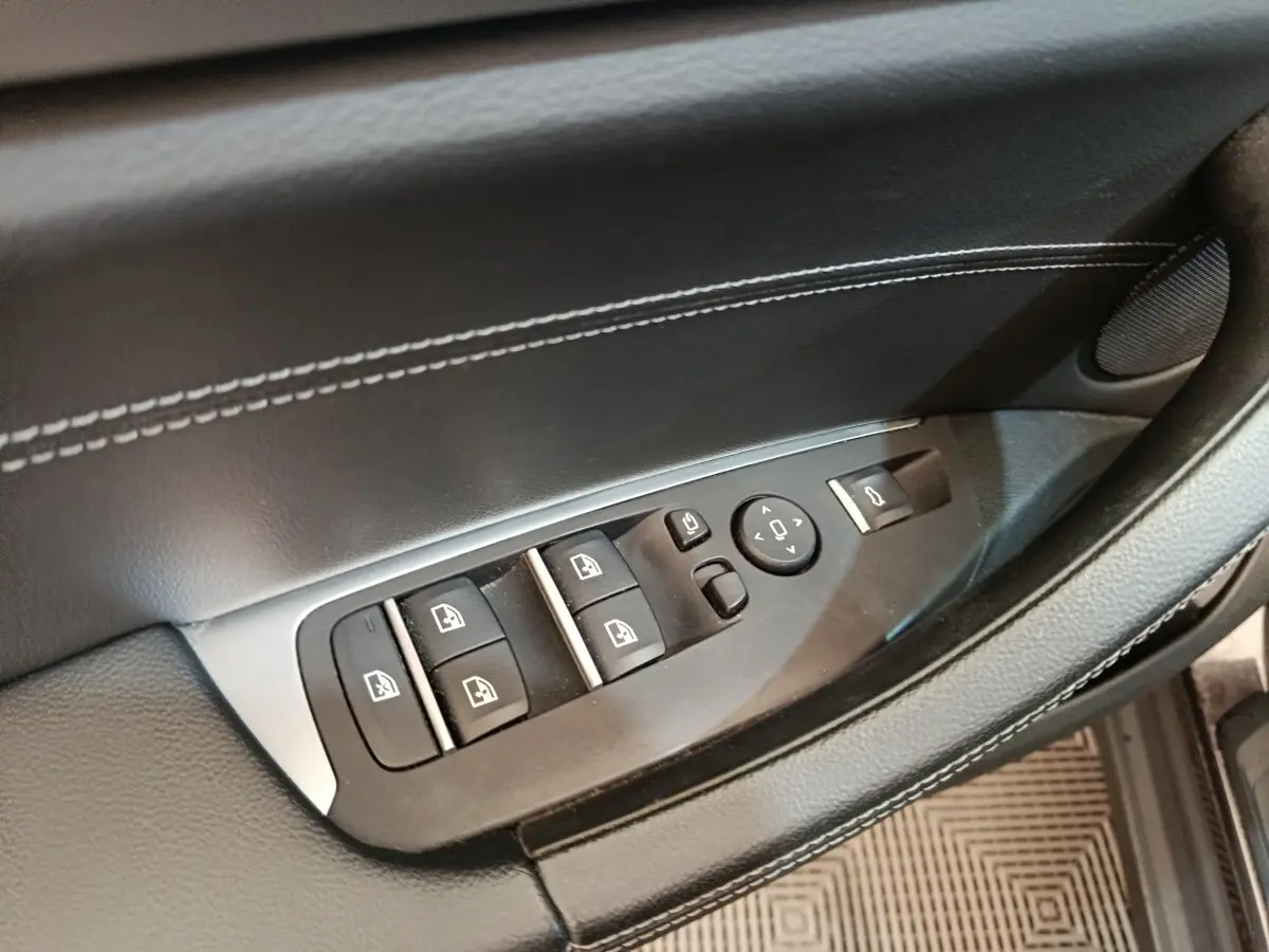 Gros plan sur la commande des vitres et rétroviseurs sur la porte côté conducteur d’un BMW X3 gris clair.