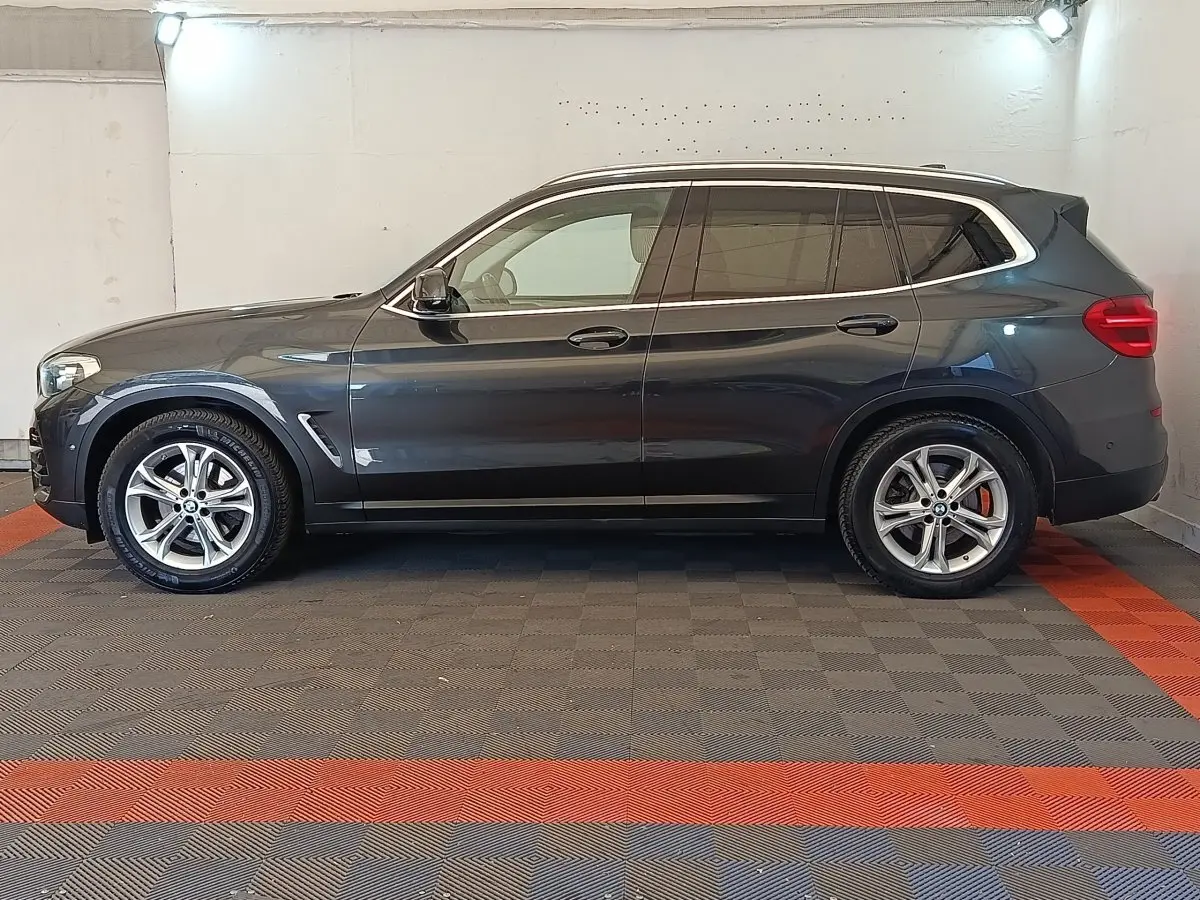 Profil côté gauche d'un BMW X3 gris clair 2020 avec jantes alliage et vitres teintées dans un garage.