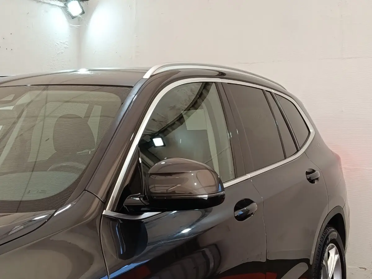Vue de profil côté gauche d'un BMW X3 gris clair avec rétroviseur et contours de vitres chromés.