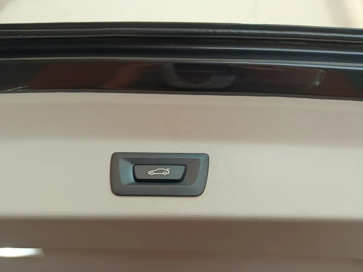Bouton d'ouverture électrique du coffre sur la garniture intérieure beige d'un BMW X3 gris clair.