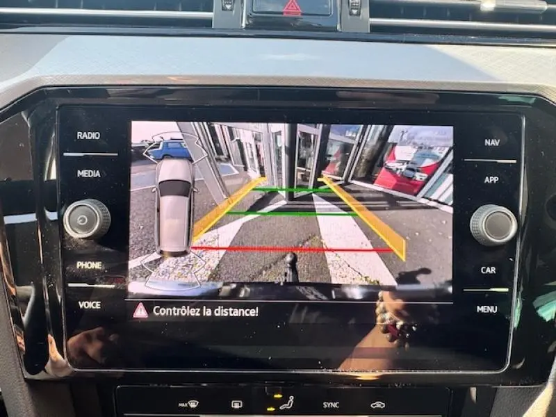 Écran de caméra de recul d'une Volkswagen Passat SW gris manganèse montrant le stationnement arrière avec lignes de guidage colorées.