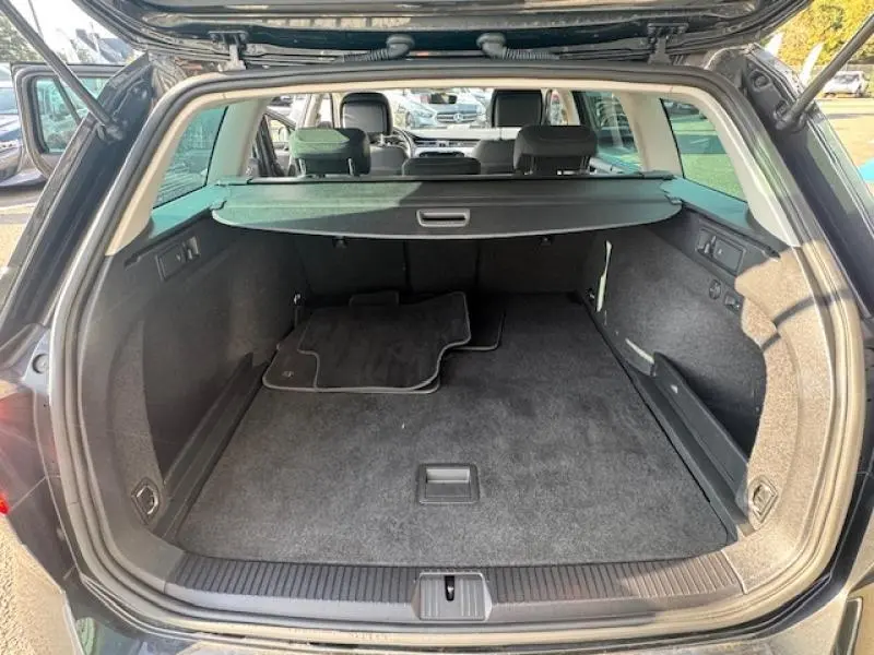 Vue arrière du coffre spacieux et propre de la Volkswagen Passat SW gris manganèse avec tapis de sol noir posé à l'intérieur.