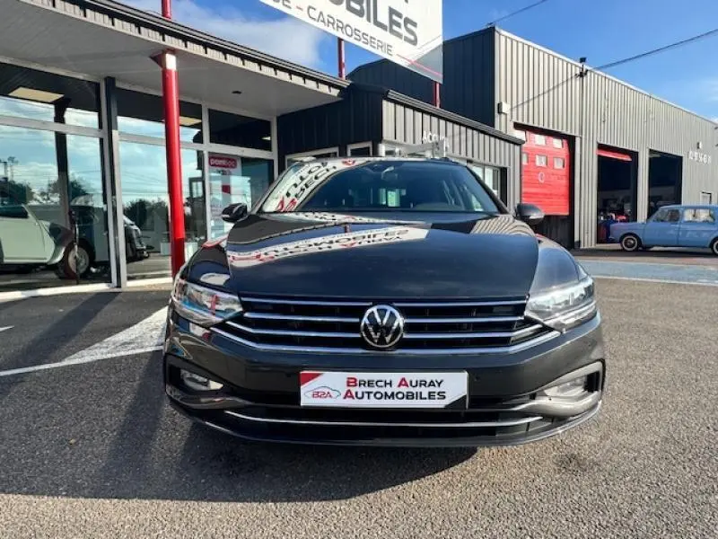 Volkswagen Passat SW gris manganèse métallisé vue de face devant un garage avec logo VW et plaque Brech Auray Automobiles.