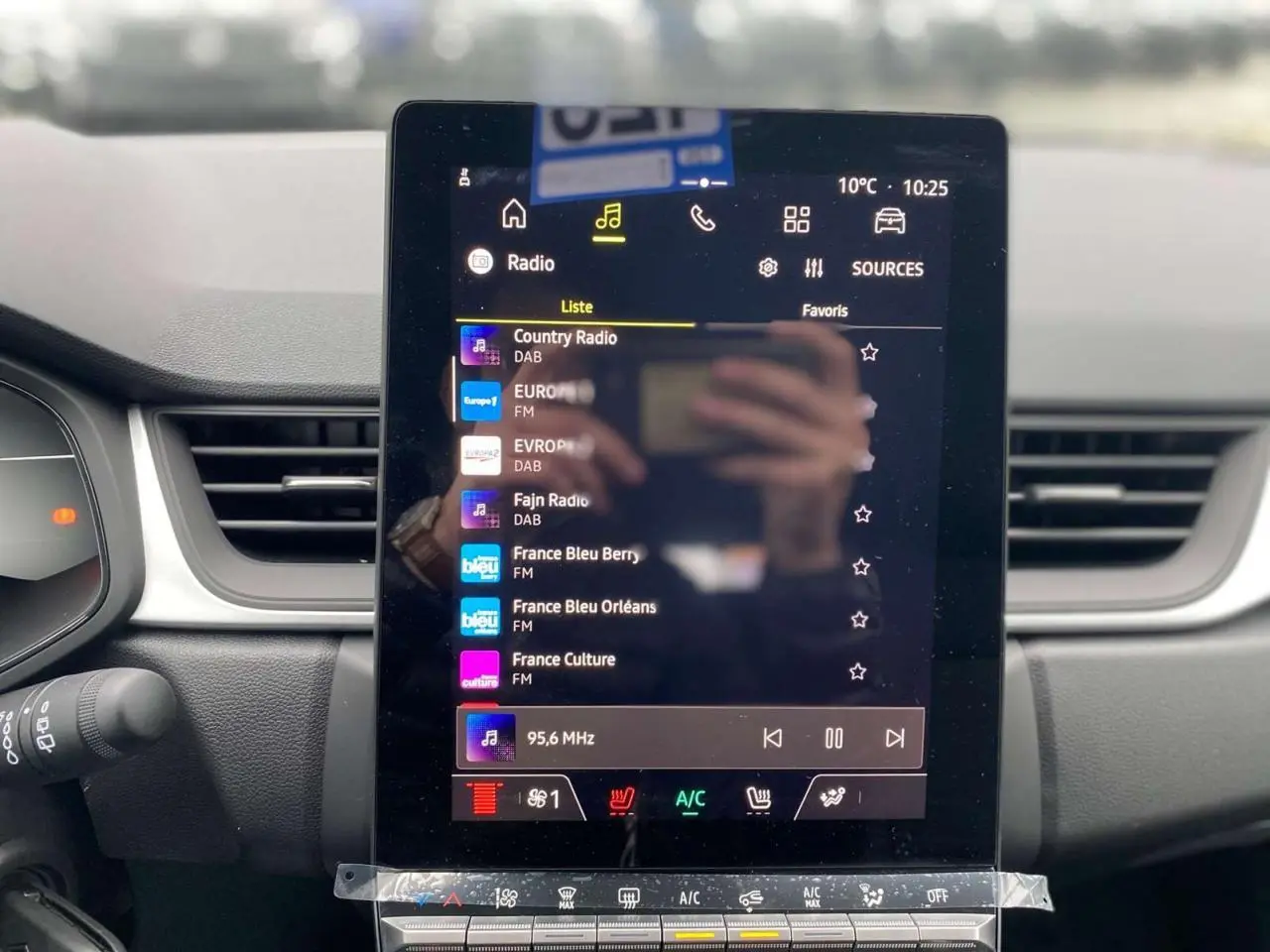 Vue rapprochée de l’écran tactile central du Renault Captur 2025 affichant la liste des radios avec commandes climatisation en dessous.