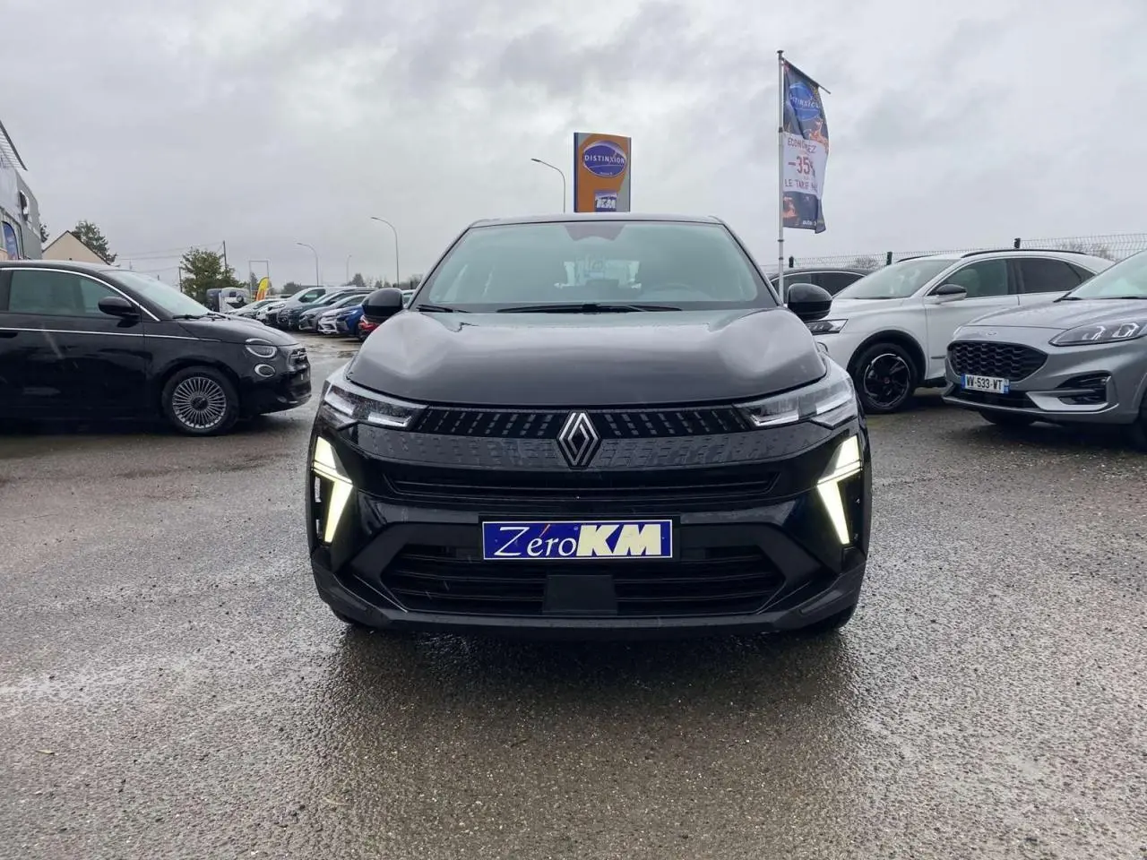 Vue avant d'un Renault Captur 2025 noir étoilé avec feux LED allumés sur un parking humide.