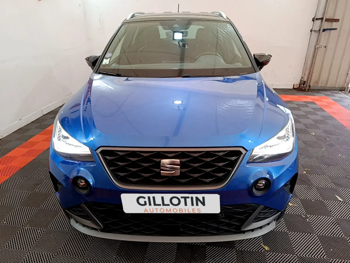 Vue avant d'une SEAT Arona bleu vif avec phares LED allumés dans un garage fermé.