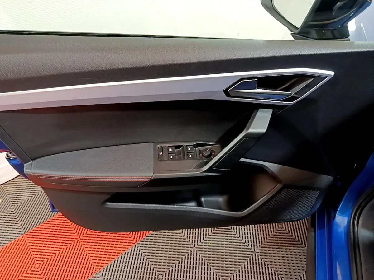 Vue intérieure côté gauche de la porte avant d’un SEAT Arona bleu 2022 avec garniture noire et surpiqûres rouges.