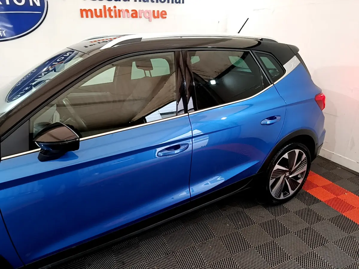 Vue de profil côté gauche d'un SEAT Arona bleu 2022 avec toit noir et jantes alliage stylisées.