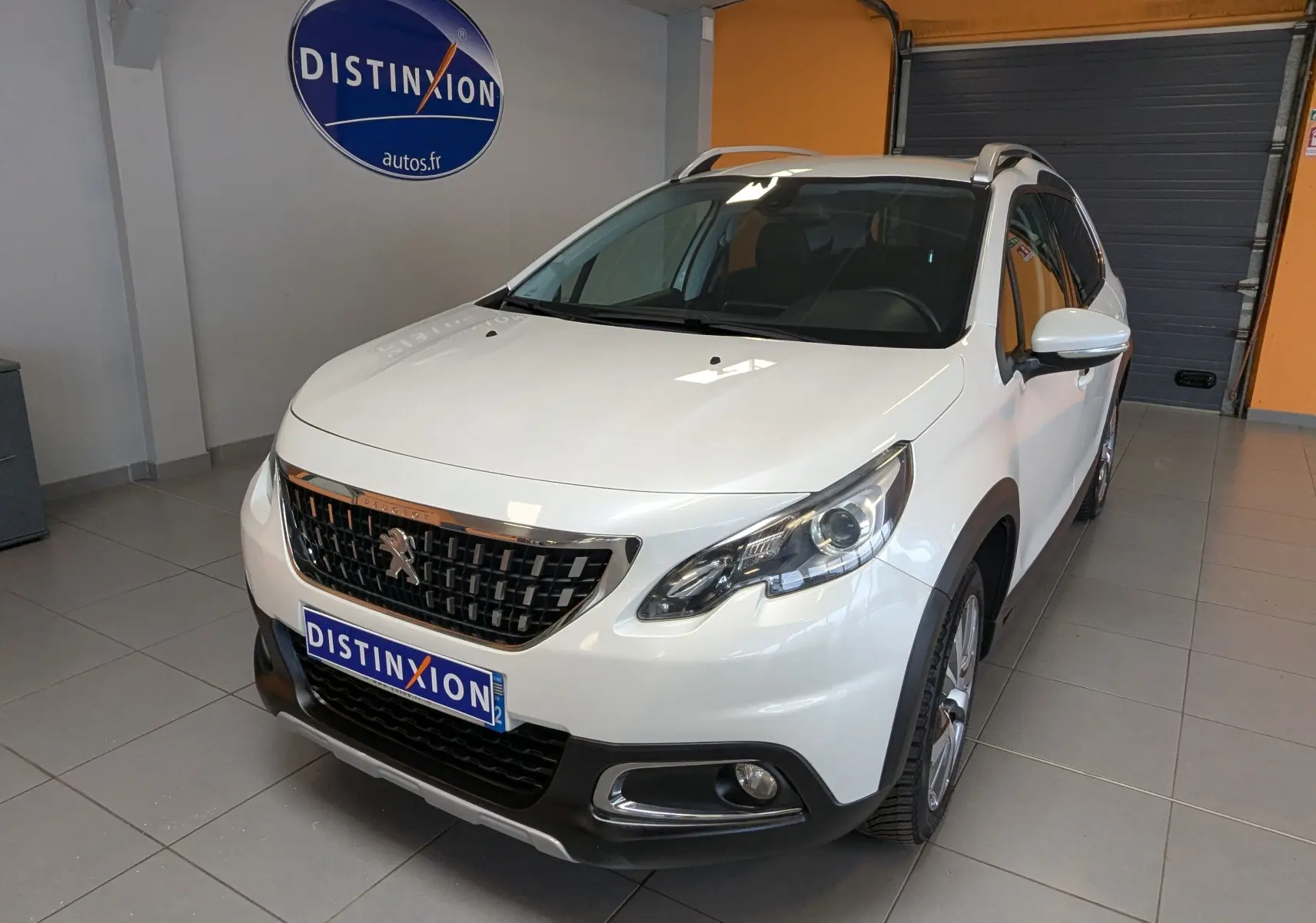 Peugeot 2008 blanc vue 3/4 avant droit en intérieur, avec calandre noire et toit ouvrant panoramique.