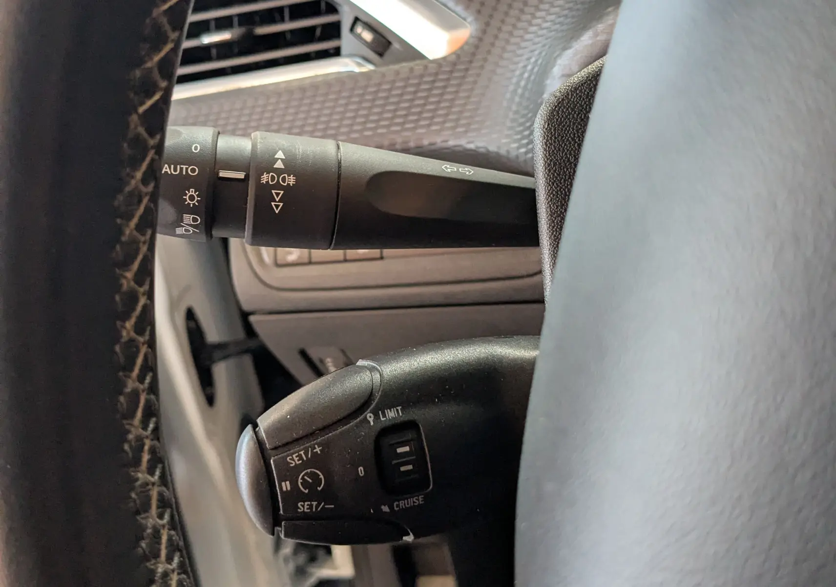 Gros plan sur les commandes de régulateur de vitesse et éclairage côté gauche du volant d’un Peugeot 2008 blanc de 2017.