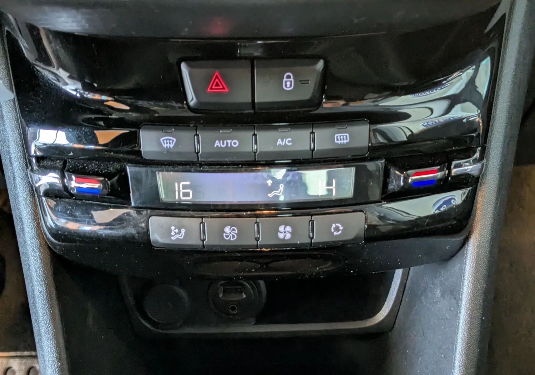 Gros plan sur la console centrale noire du Peugeot 2008 blanche, montrant les commandes de climatisation digitale et boutons de sécurité.
