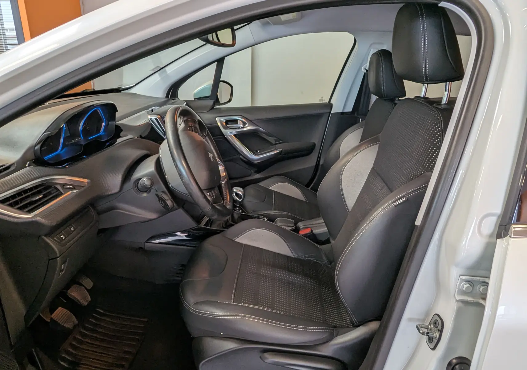 Vue intérieure côté conducteur de la Peugeot 2008 blanche, mettant en valeur les sièges noirs et gris et le tableau de bord moderne.