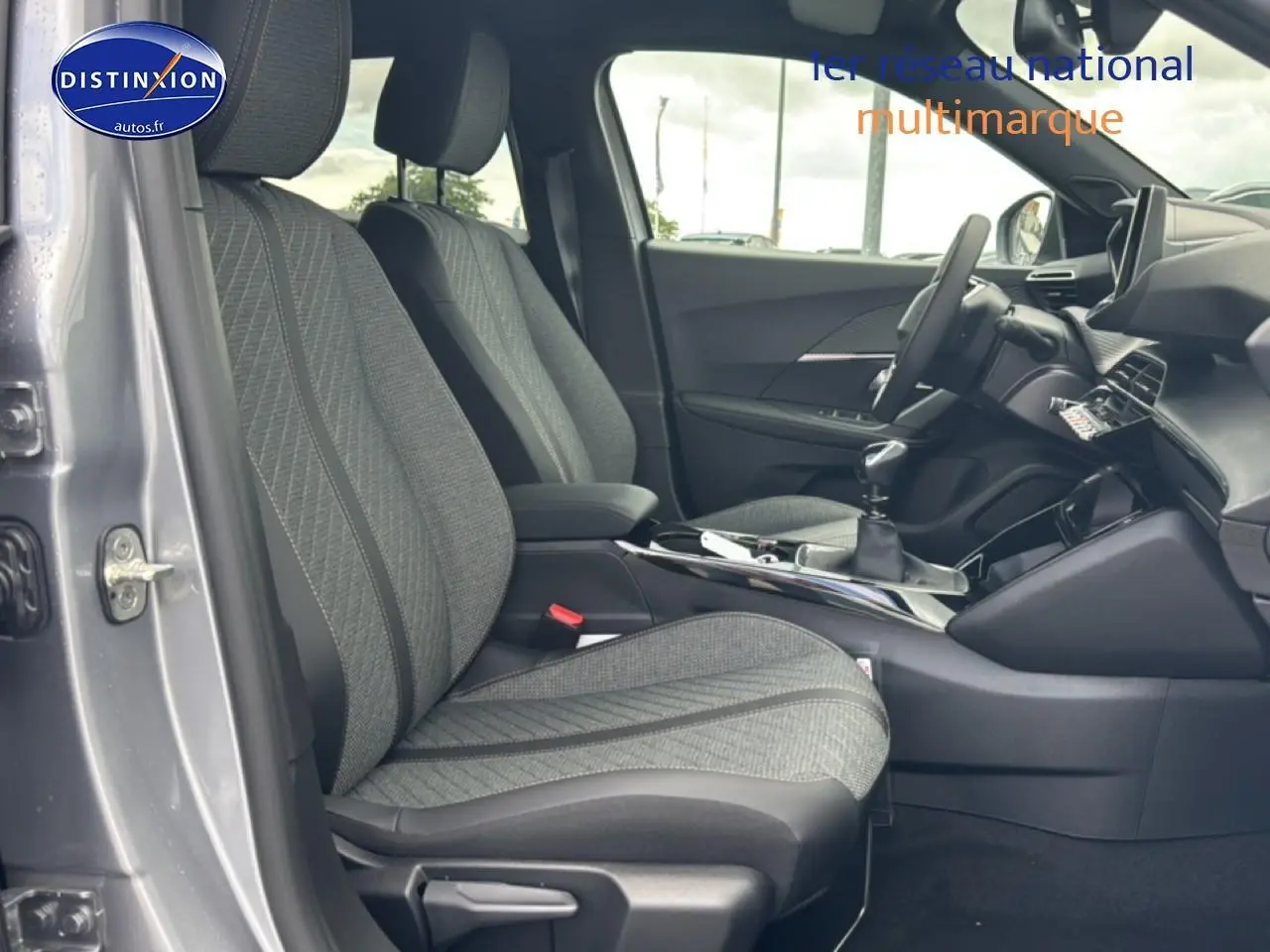 Vue intérieure côté conducteur du Peugeot 2008 gris artense, mettant en valeur les sièges en tissu et la boîte manuelle.