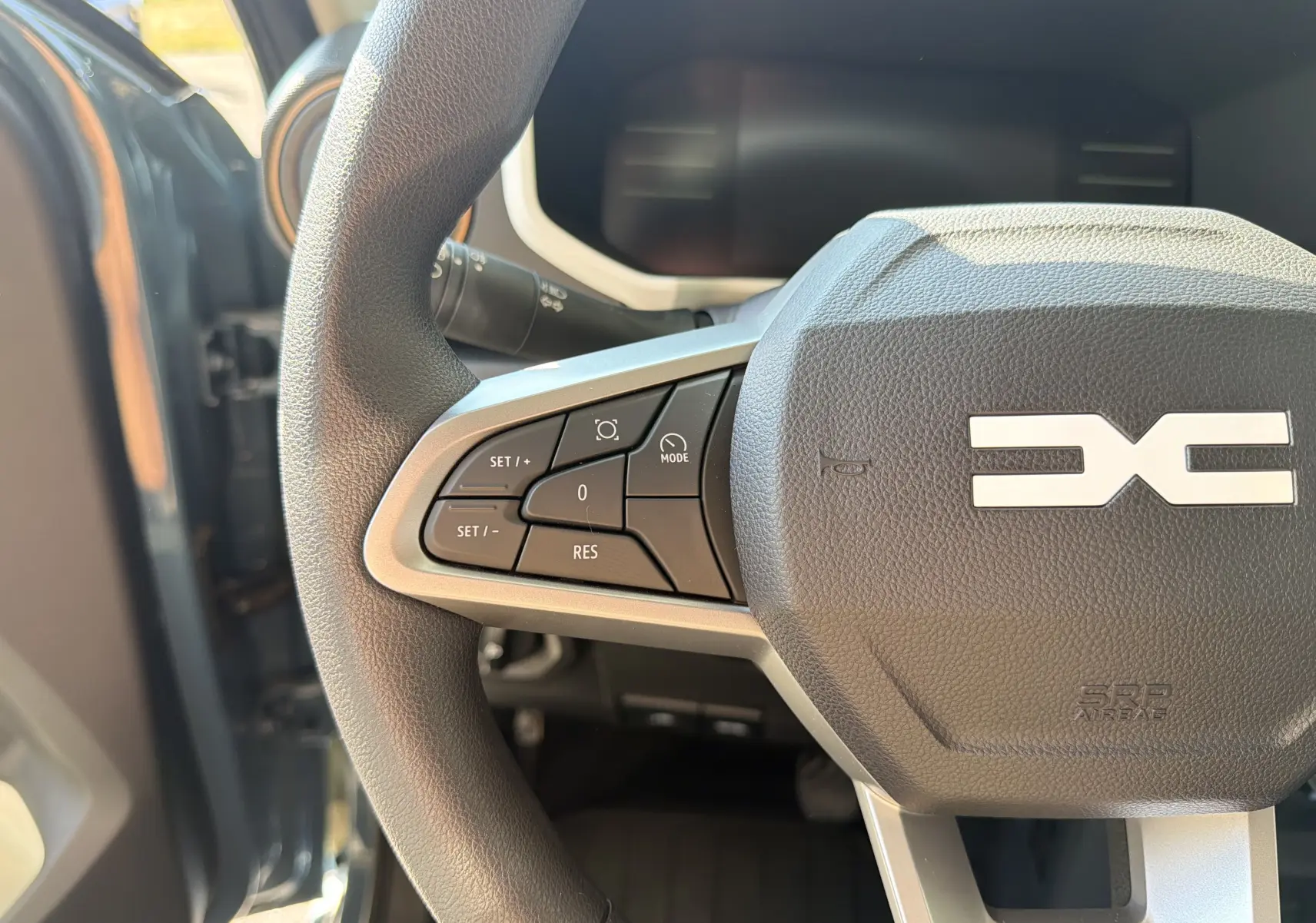 Gros plan sur le volant du Dacia Spring 65 Extreme 2026, montrant les commandes à gauche et le logo central en relief.