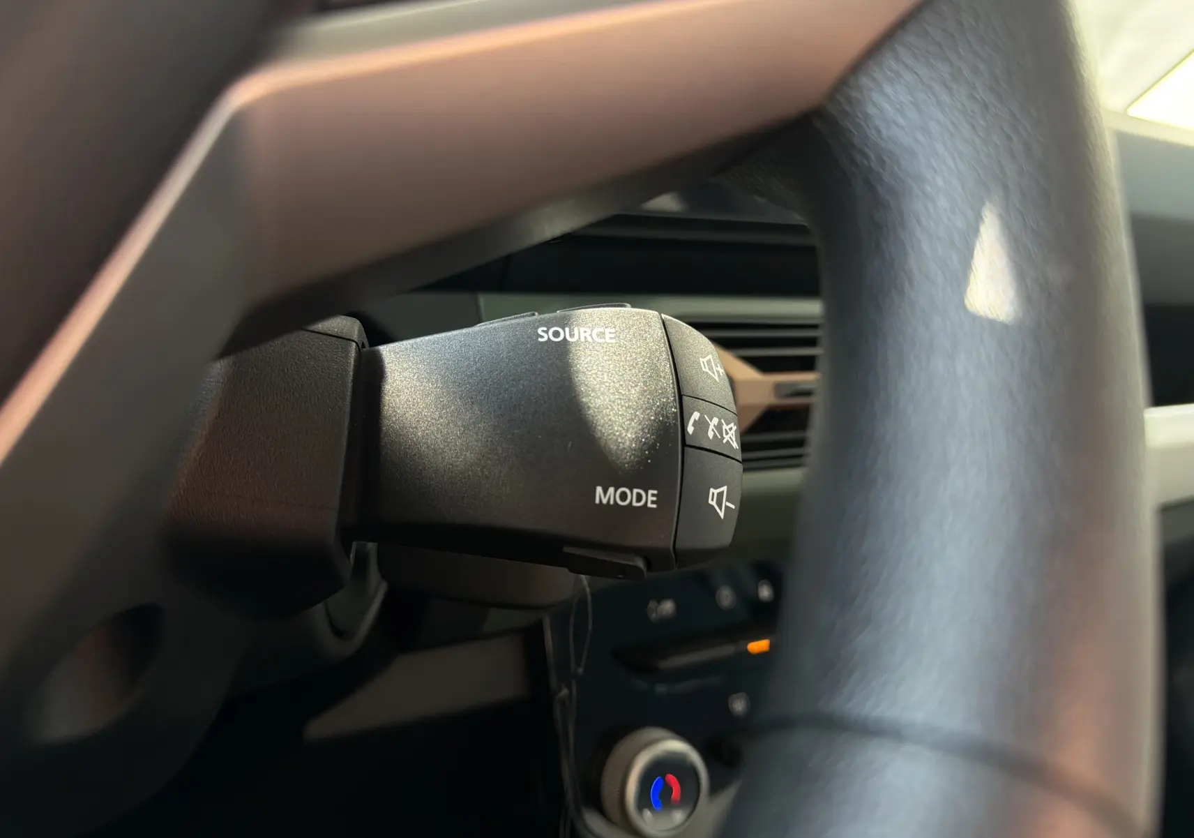 Gros plan sur la commande au volant du DACIA Spring 65 Extreme 2026, avec boutons source et mode visibles, intérieur noir.