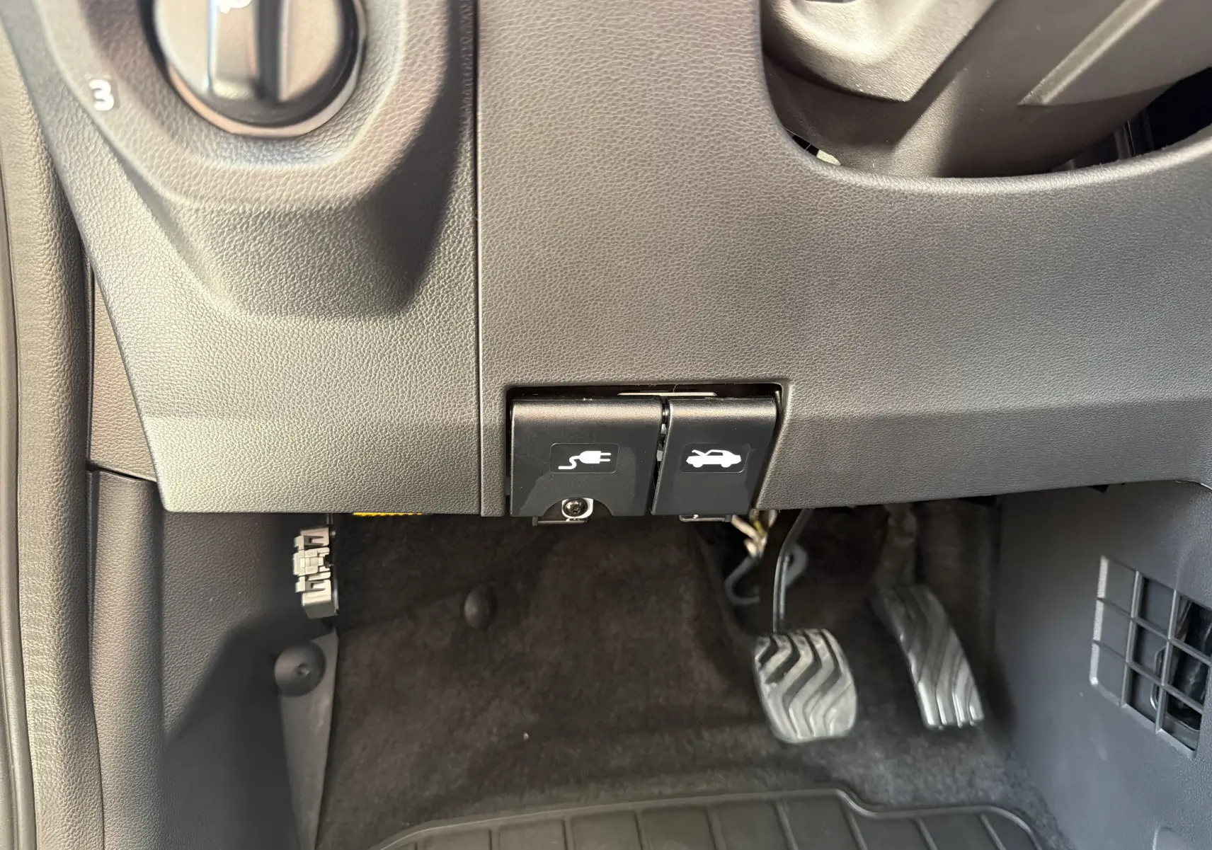 Gros plan sur les commandes d'ouverture du capot et de la trappe de recharge électrique sous le tableau de bord d'une Dacia Spring 65 Extreme 2026.
