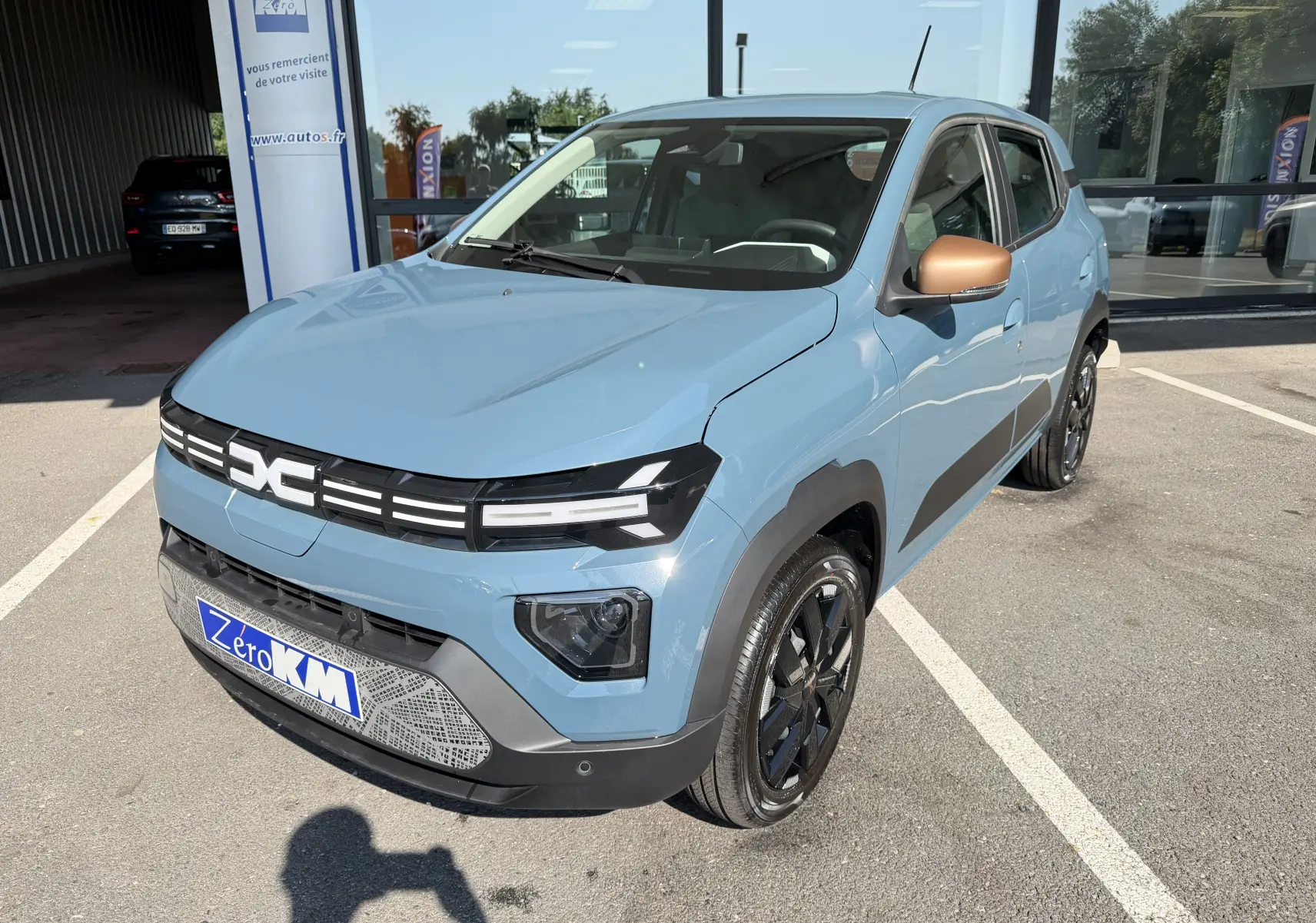 Dacia Spring 65 Extreme bleu ardoise en 3/4 avant droit, avec rétroviseurs bronze et jantes noires brillantes.