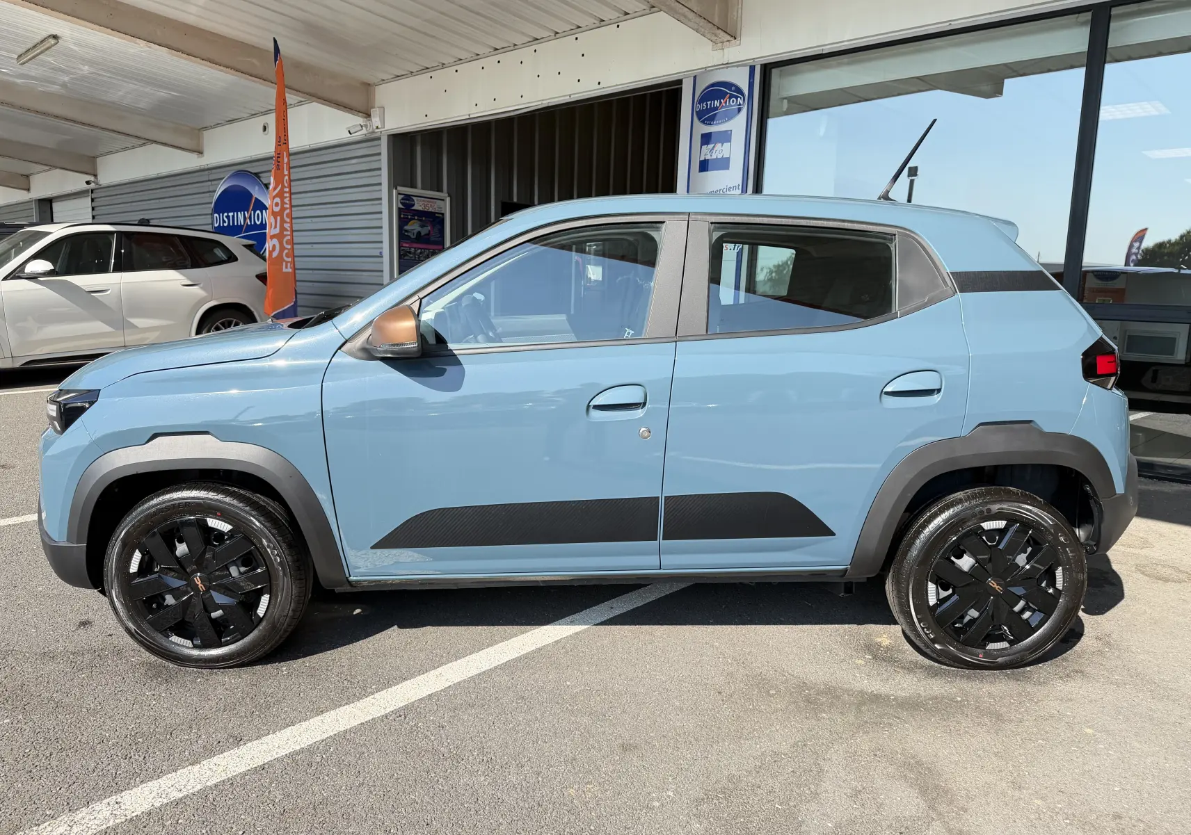 Vue de profil côté gauche d'une Dacia Spring 65 Extreme 2026 bleu ardoise avec jantes noires et protections latérales noires.