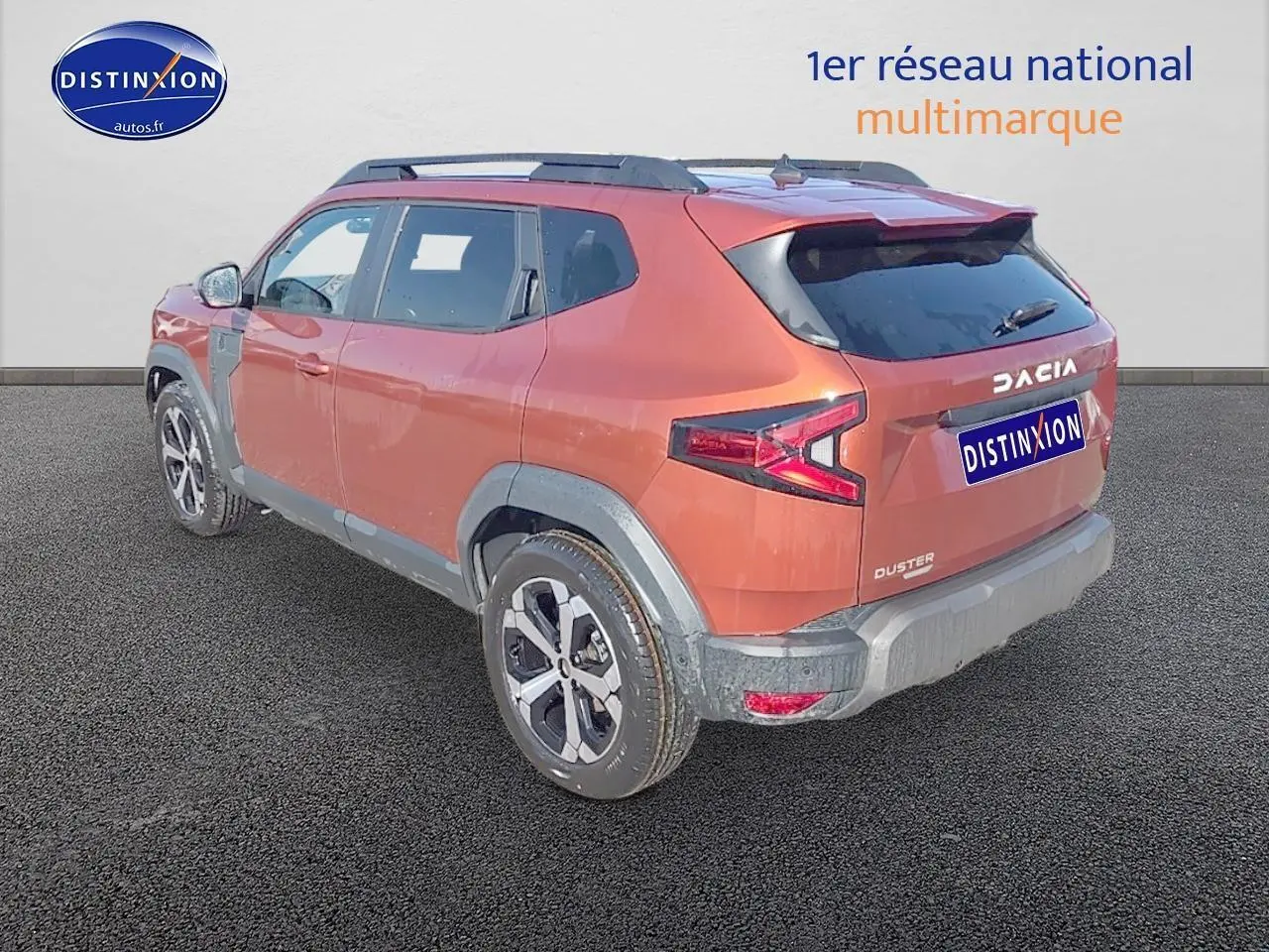 Vue 3/4 arrière droit du Dacia Duster brun terracotta avec barres de toit et jantes alu distinctives.