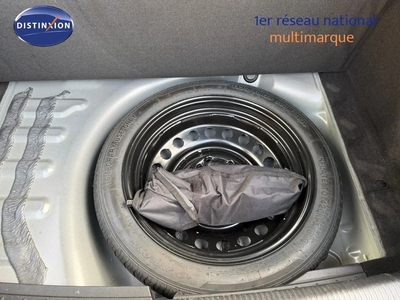 Roue de secours noire dans le coffre d'une Peugeot 508 gris platinium, vue plongeante sur le pneu et son sac d'outils.