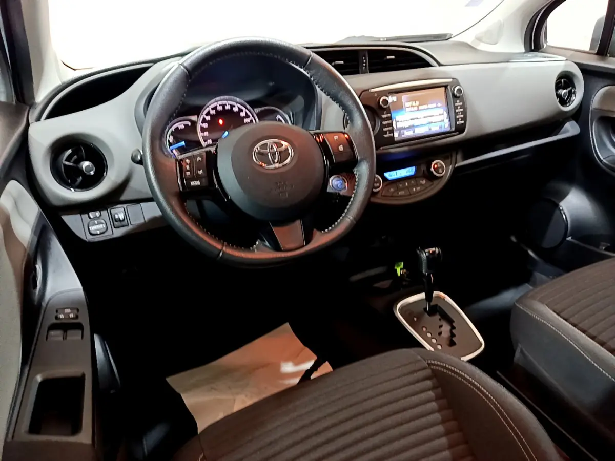 Vue intérieure de la Toyota Yaris 2020, tableau de bord et volant cuir noir avec écran tactile central allumé.
