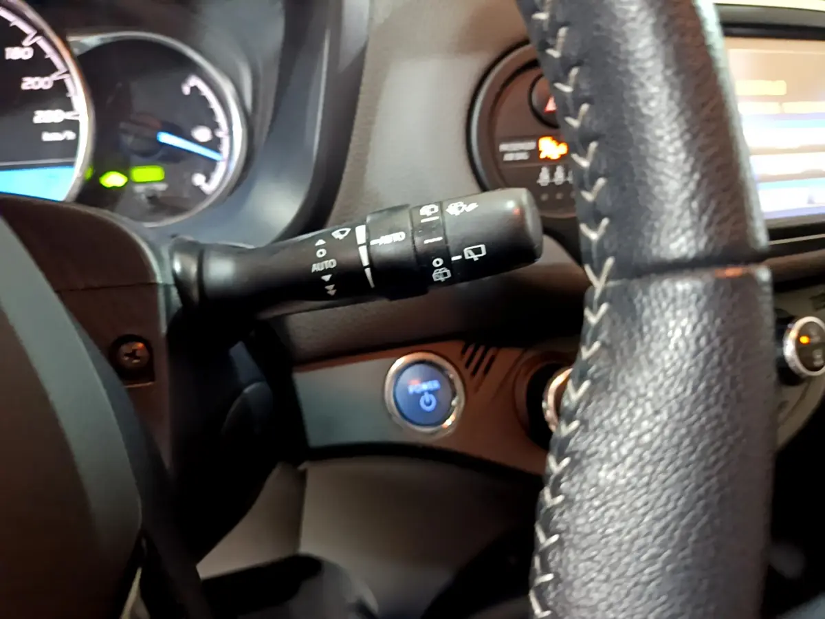 Vue intérieure rapprochée du volant noir et du bouton démarrage bleu de la Toyota Yaris blanche hybride 2020.