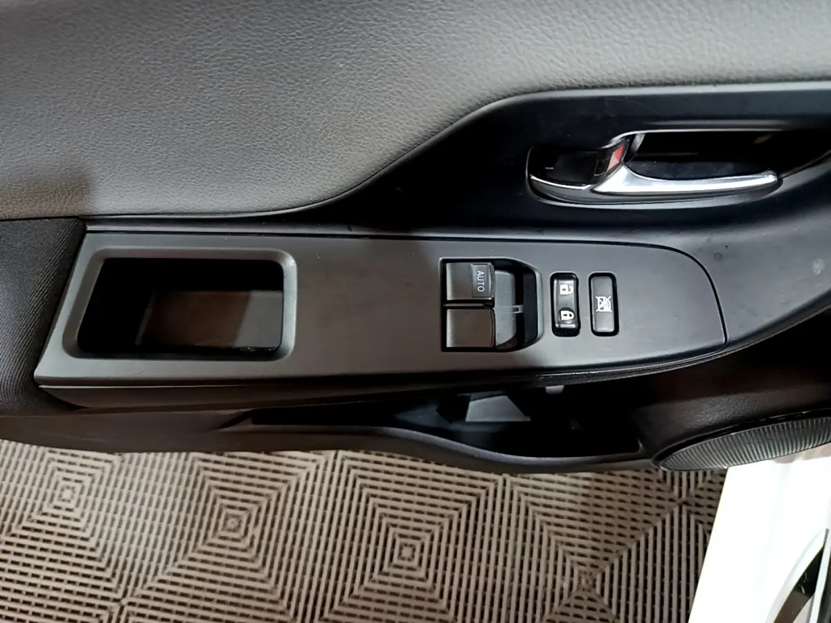 Détail de la porte intérieure côté conducteur de la Toyota Yaris blanche, montrant les commandes des vitres et la poignée chromée.