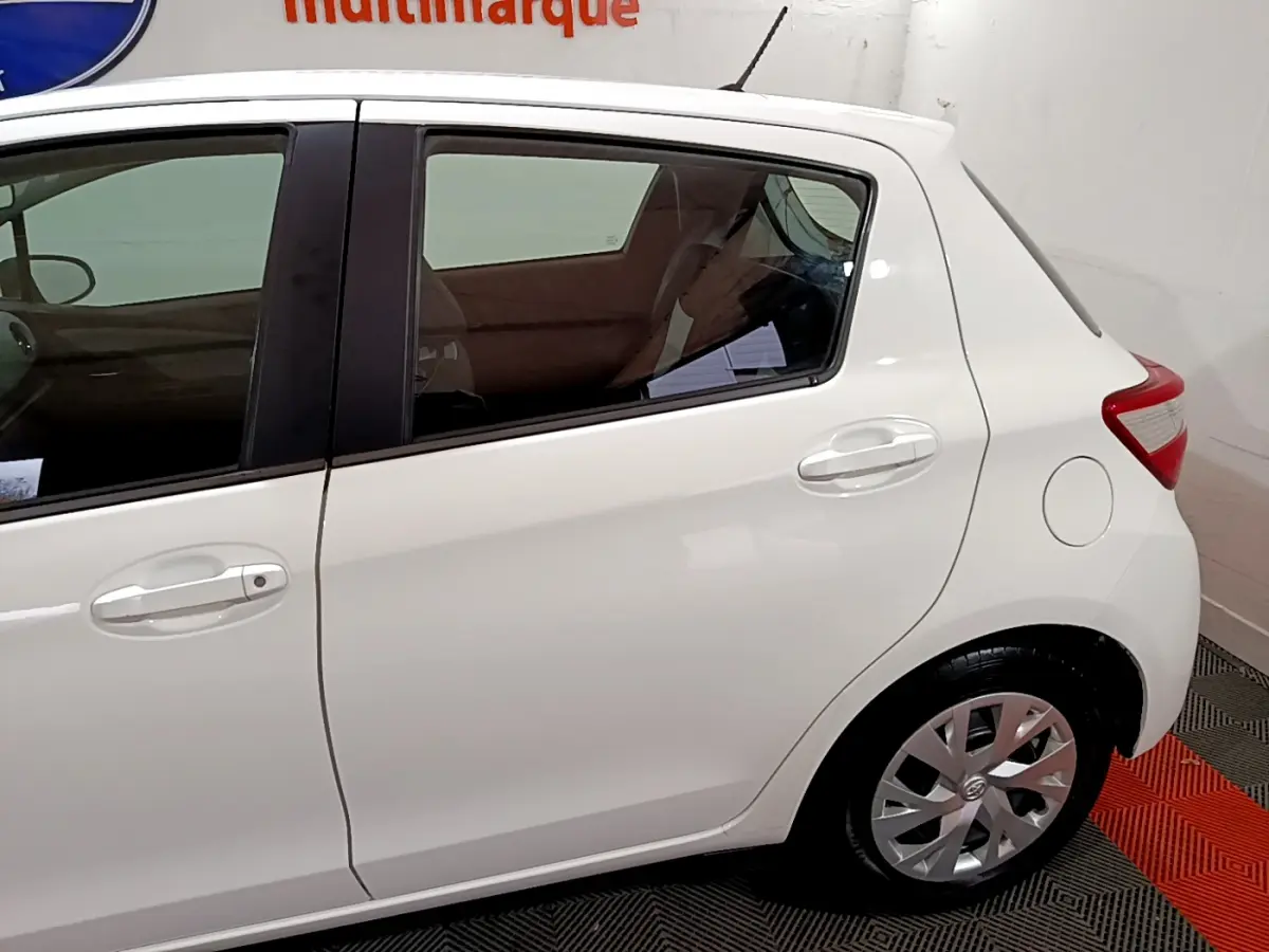 Vue latérale côté droit de la Toyota Yaris blanche 1.5 Hybride 2020, mettant en valeur la porte arrière et la roue arrière.