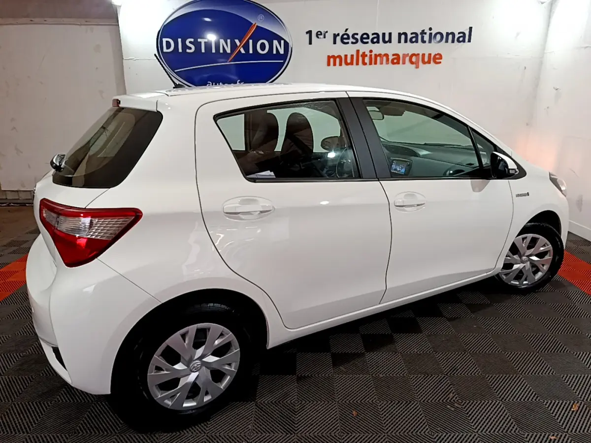 Vue de profil côté gauche d'une Toyota Yaris blanche 1.5 Hybride 100h France Business de 2020 en intérieur showroom.