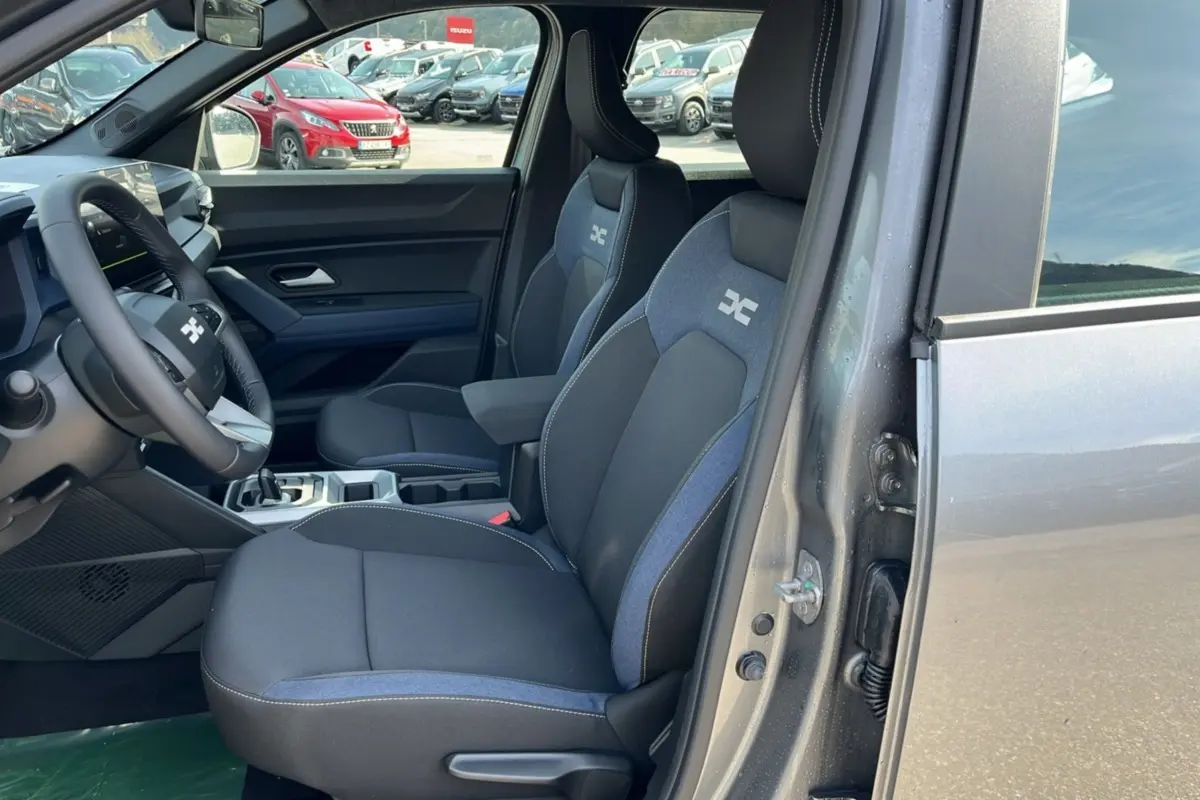 Vue intérieure côté conducteur du Dacia Bigster Hybrid 155 Expression Plus gris schiste, avec sièges tissu bicolore et volant cuir.