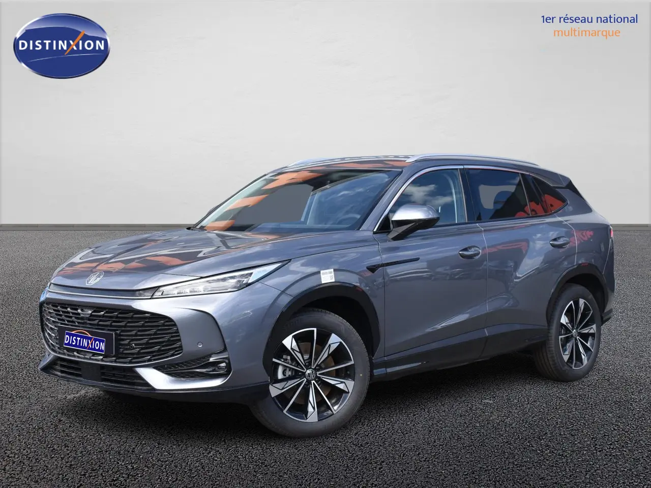 MG Motor EHS gris en 3/4 avant droit, avec jantes alliage noires et phares LED fins, sur fond neutre.