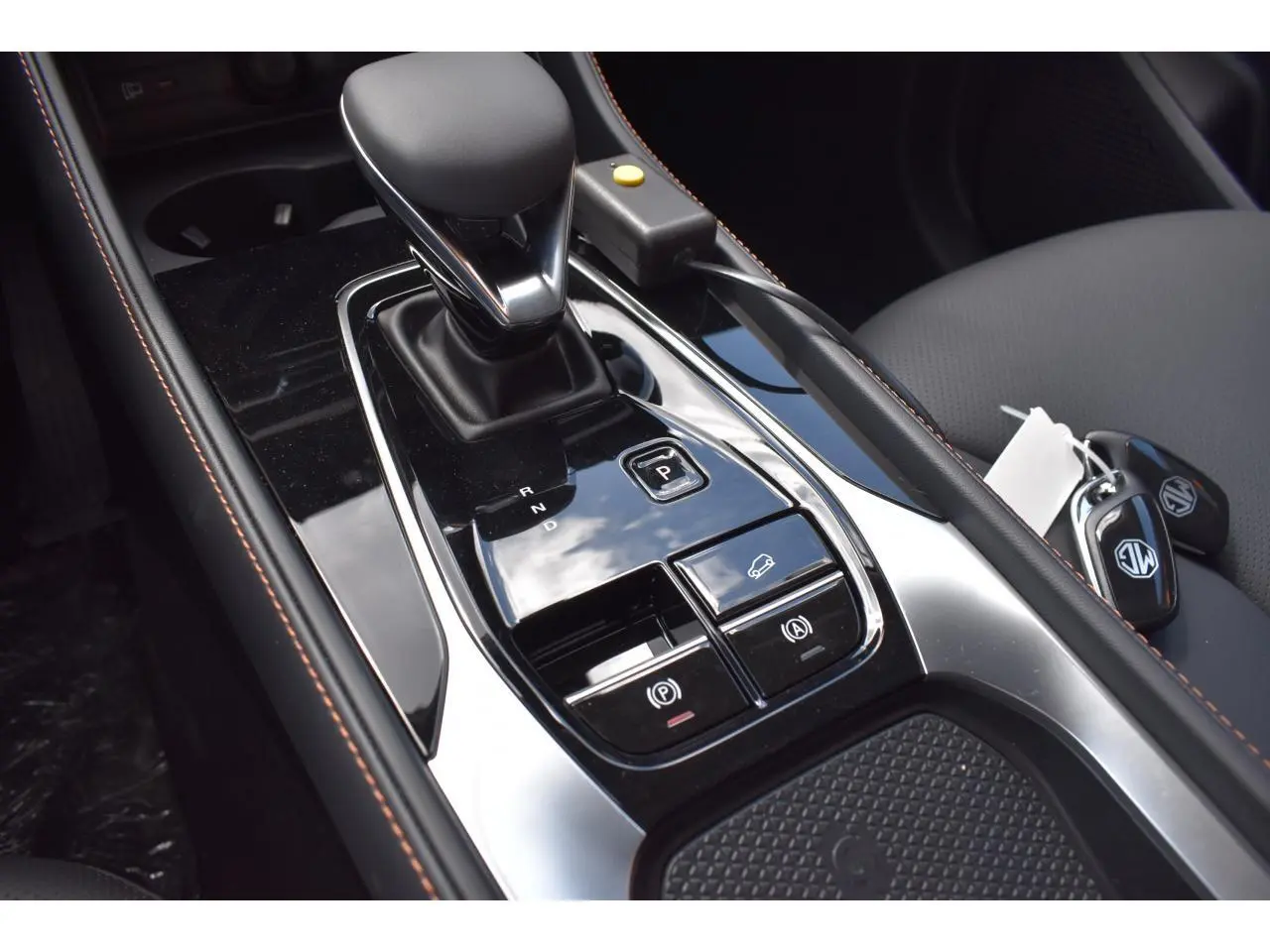 Gros plan sur la console centrale noire brillante du MG Motor EHS gris, avec levier de vitesse automatique et clés sur siège.