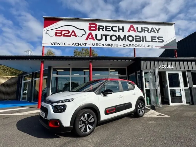 Citroën C3 1.2 83ch Shine vue 3/4 avant droit en blanc Banquise avec toit et détails rouges devant concession Brech Auray Automobiles