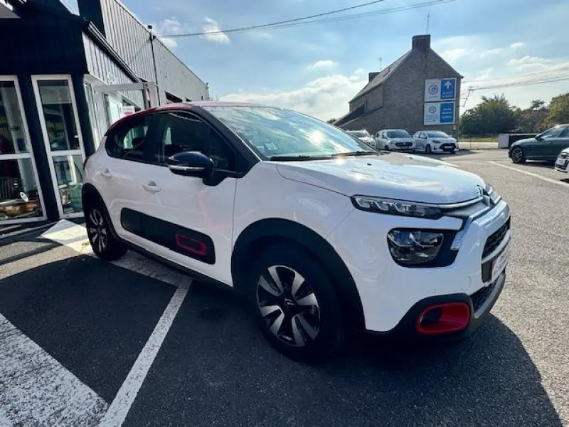 Citroën C3 2021 blanc Banquise avec toit et détails rouges, vue 3/4 avant droit en extérieur devant un bâtiment.