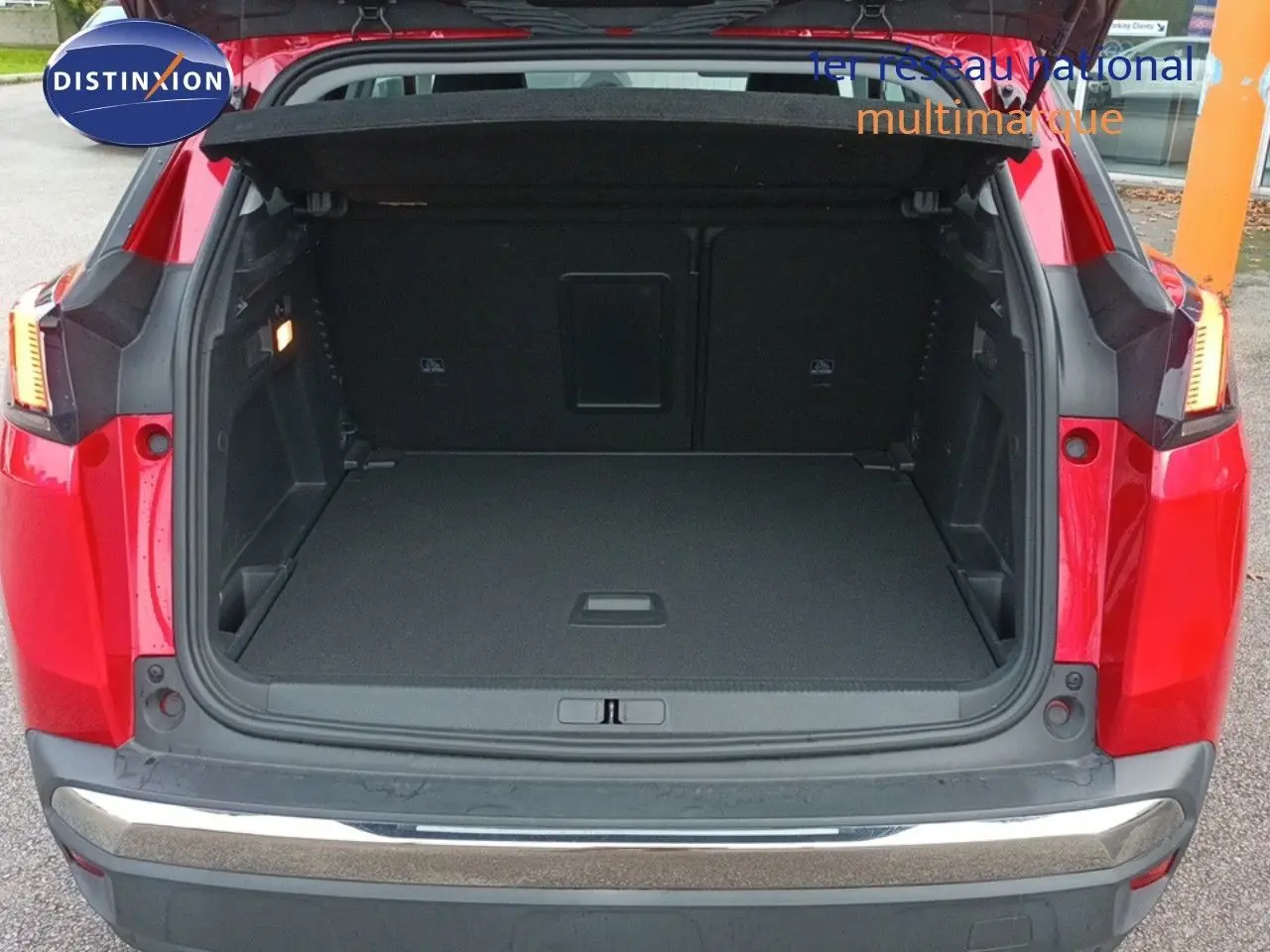 Coffre ouvert d'un Peugeot 3008 rouge foncé métal vu de l'arrière, montrant l'espace de chargement vide et les feux arrière allumés.
